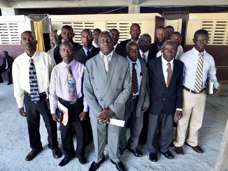 A group of adult men, students of a Bible training program in Haity, wearing suits, are posing for a picture