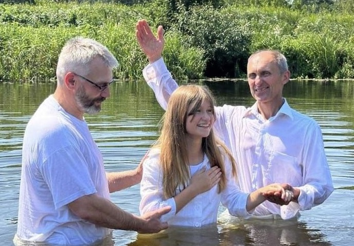 Two ministers in Ukraine are baptizing a young lady in the river in the summer